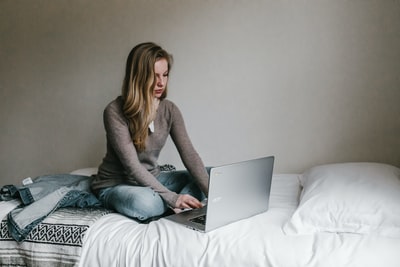 女人坐在房间的床上，在MacBookPro上打字